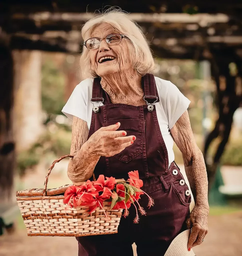 Eine fröhliche Seniorin im Garten mit einem Korb voller Blumen als Beispiel für die Förderung der Mobilität im Alltag.