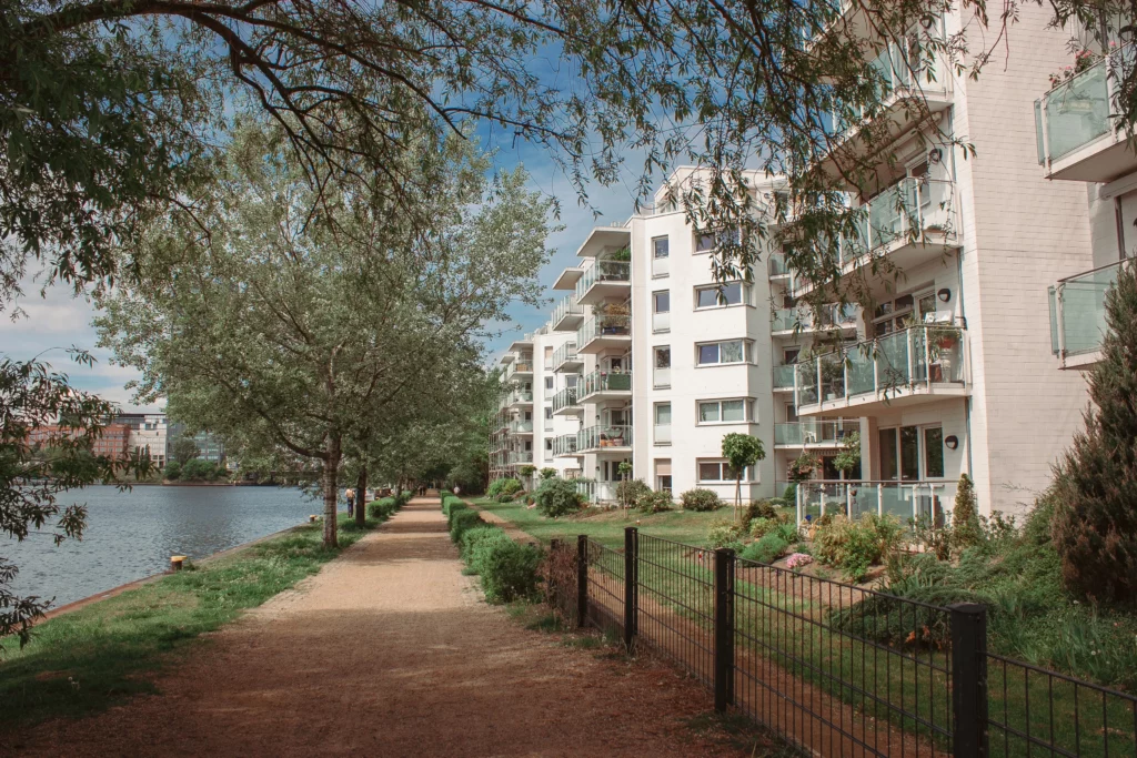 Moderne Wohnanlage am Wasser f&uuml;r die Pflegeberatung Berlin-Lichtenberg mit sonnigem Uferweg und gr&uuml;nen B&auml;umen