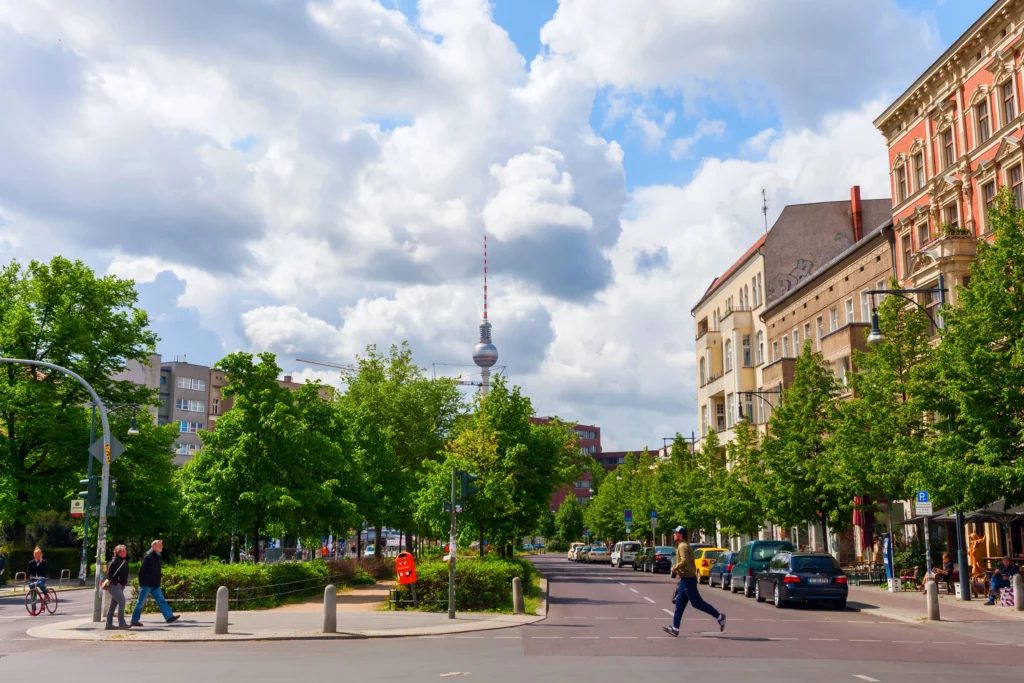 Belebtes Straßenviertel für die Pflegeberatung Berlin-Pankow mit grünen Bäumen, Altbau-Fassaden und dem Fernsehturm
