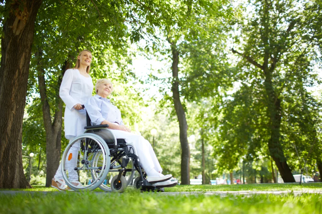 Professionelle Seniorenbetreuung Berlin-Marzahn: Eine Pflegekraft begleitet eine Seniorin im Rollstuhl durch einen Park.